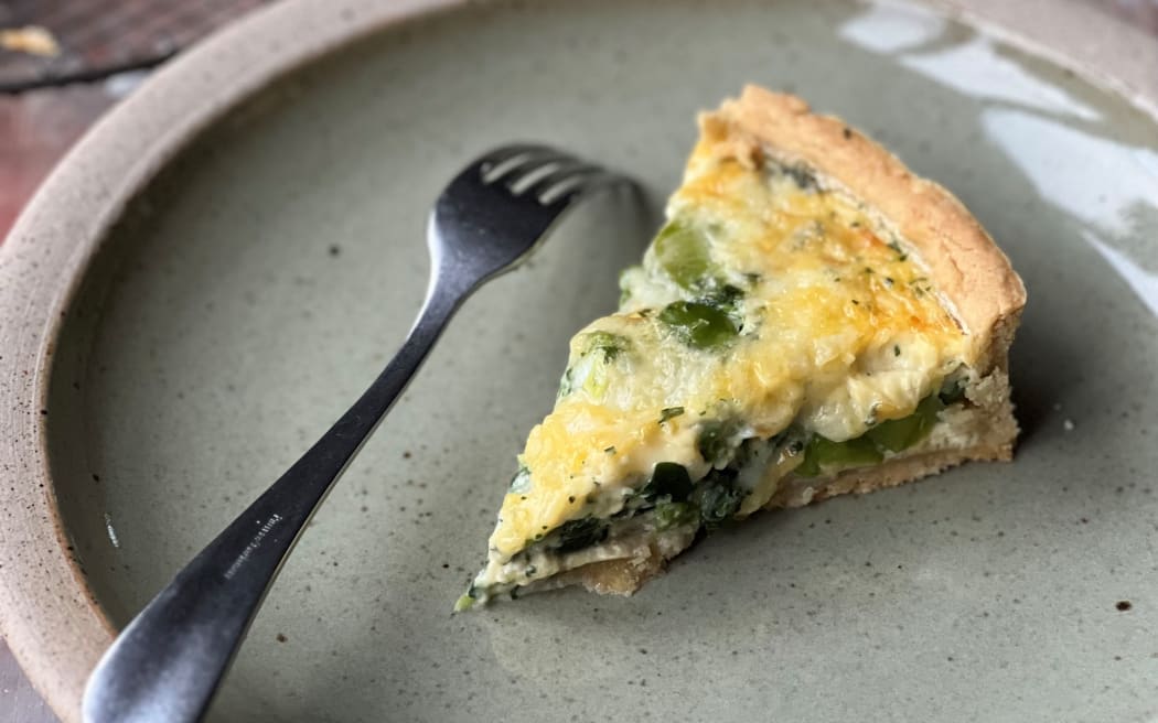 A slice of quiche on a plate. Green beans and spinach is visible among the creamy egg mixture.