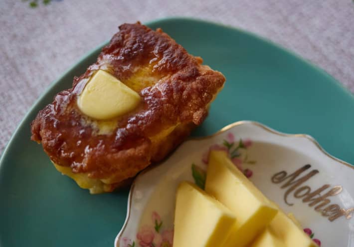A mini loaf of fry bread is buttered and sitting on a green plate.