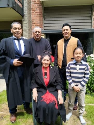 Dr Timoti Te Moke wearing his graduation gown, stands with his whānau.