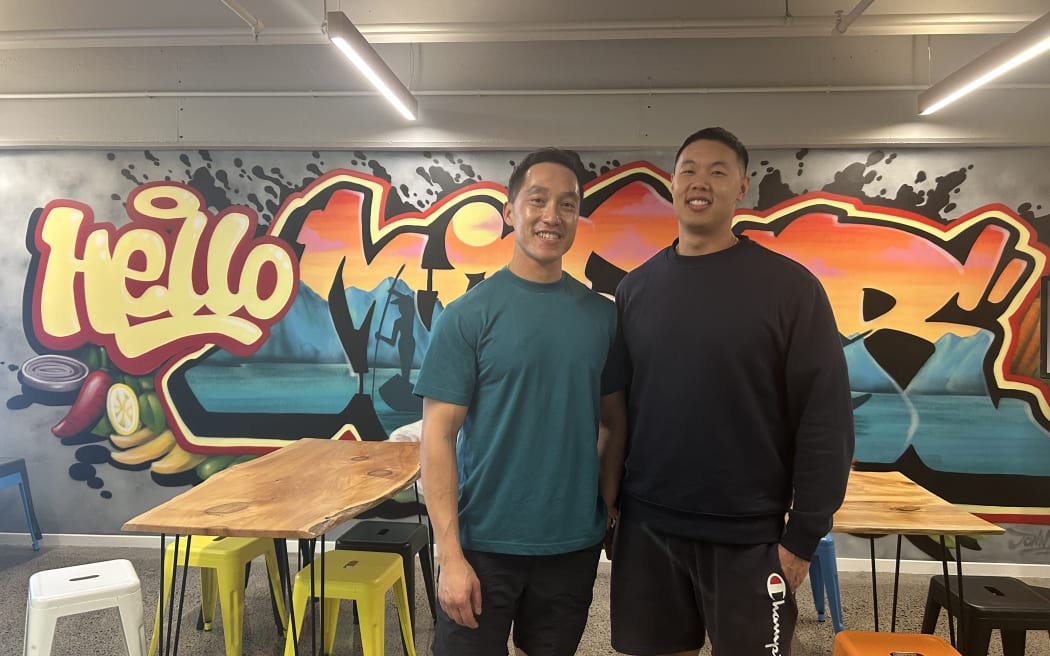 A photo of two people standing in front of a mural in a restaurant.