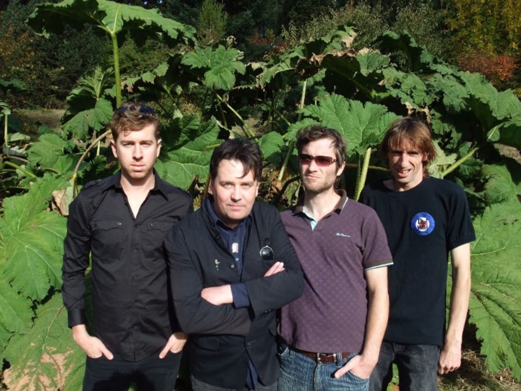The Chills band members standing in front of a plant