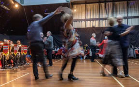 An auditorium full of couples dancing. The band sits to the side, playing.