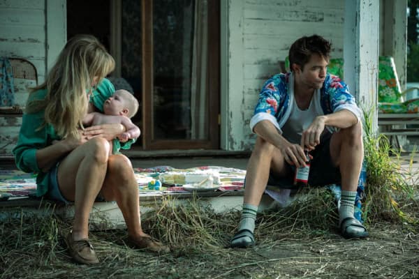 A young couple, with the woman holding a baby, sit on the front deck of a house.