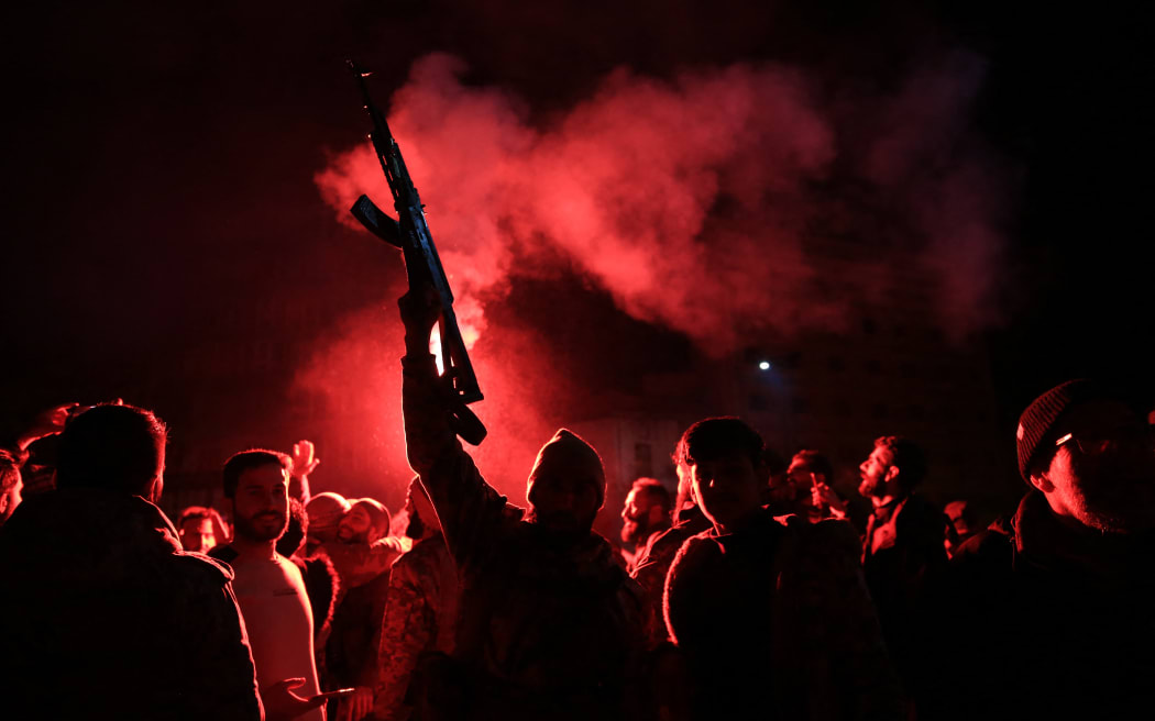 Rebel forces shoot in the air as they celebrate in the central Syrian city of Homs early on December 8, 2024, after they entered Syria's third city overnight. - Hayat Tahrir al-Sham (HTS) and allied anti-goovernment factions have pressed a lightning offensive since November 27, sweeping swathes of the country from government control, including major cities Aleppo, Hama, Homs and the capital Damascus. (Photo by Aref TAMMAWI / AFP)