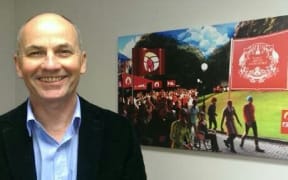 Glenn stands in front of  an art work of a PSA protest