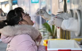A health worker takes a swab sample from a woman to test for the Covid-19 coronavirus in the Jing'an district in Shanghai on December 22, 2022. (Photo by Hector RETAMAL / AFP)