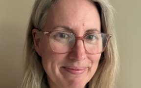 This is a head shot of Kristen O'Connor. She is wearing glasses, has shoulder length blonde hair, and looks towards the camera on a slight angle.