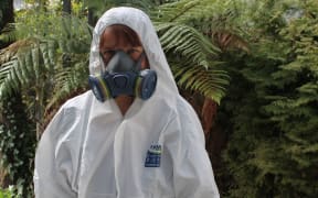 A photo of Katy Gosset wearing a mark and white protective suit and hood, ready to go into a meth house.