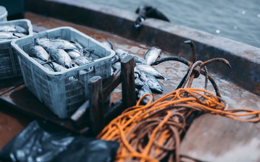 View with a shallow depth of field of the deck of a fishing vessel: boxes with a fresh fish yield of tuna, the yellow rope and simple drag anchor, ocean water with bokeh overboard