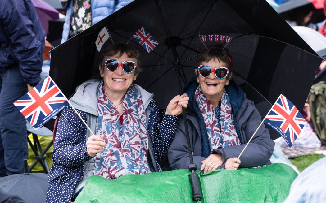 Well-wishers protect themselves against the rain as they wait along the route of the 'King's Procession', a two kilometres stretch from Buckingham Palace to Westminster Abbey, as they wait for Britain's King Charles III and Britain's Camilla, Queen Consort to pass in the Diamond State Coach, in central London, on May 6, 2023 ahead of their coronations. - The set-piece coronation is the first in Britain in 70 years, and only the second in history to be televised. Charles will be the 40th reigning monarch to be crowned at the central London church since King William I in 1066. Outside the UK, he is also king of 14 other Commonwealth countries, including Australia, Canada and New Zealand. Camilla, his second wife, will be crowned queen alongside him and be known as Queen Camilla after the ceremony. (Photo by Niklas HALLE'N / AFP)