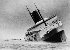 The Wahine lists heavily to starboard in Wellington Harbour. Lifeboats are just visible on the left.