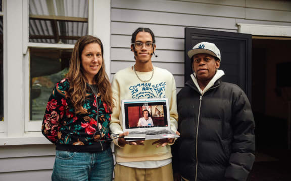 (L-R) Mara, Jamil, and Beto pose for a photo with Jamil holding a laptop where his sister Jazz is video calling in