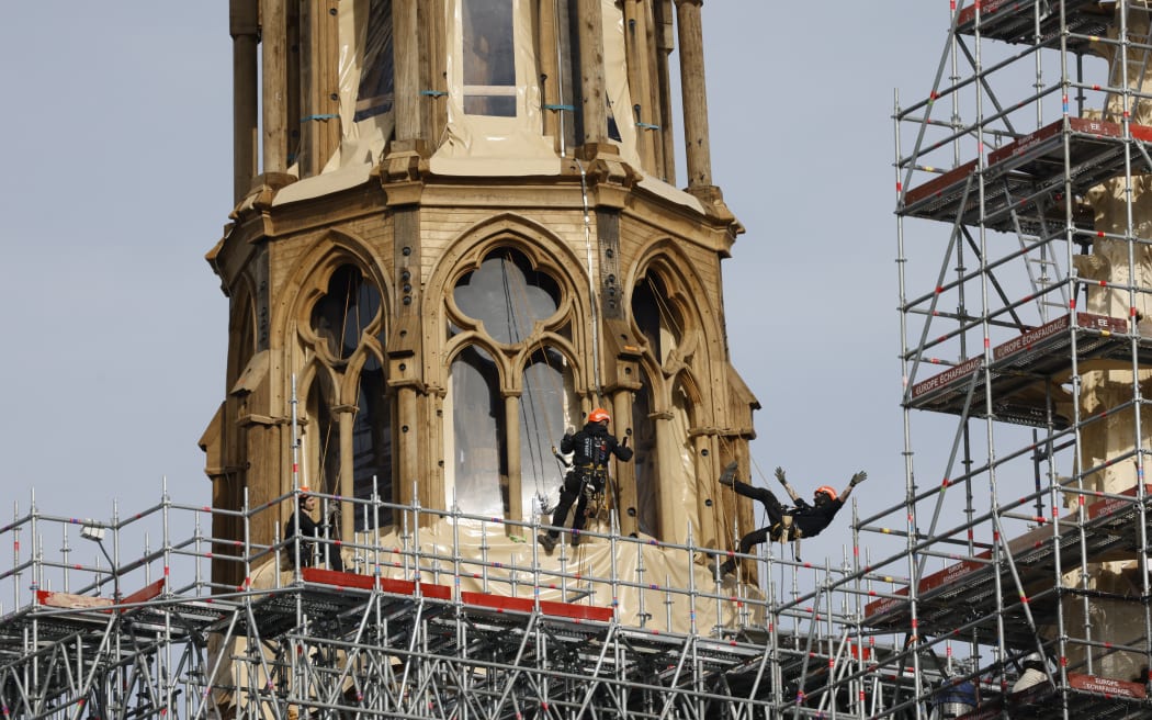 (FILES) Workers take a picture as they operate on the reconstruction of the Notre-Dame de Paris Cathedral's new wooden spire partially covered in lead in Paris on March 14, 2024. A huge fire swept through the roof of the famed Notre-Dame Cathedral in central Paris on April 15, 2019, and five years later, the reconstruction advances in its final stages before the reopening planned for the end of the year. (Photo by Ludovic MARIN / AFP)