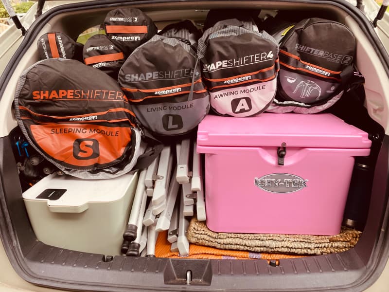 Duffle bags sit neatly on top of containers, tent poles and chilly bin in a car boot.
