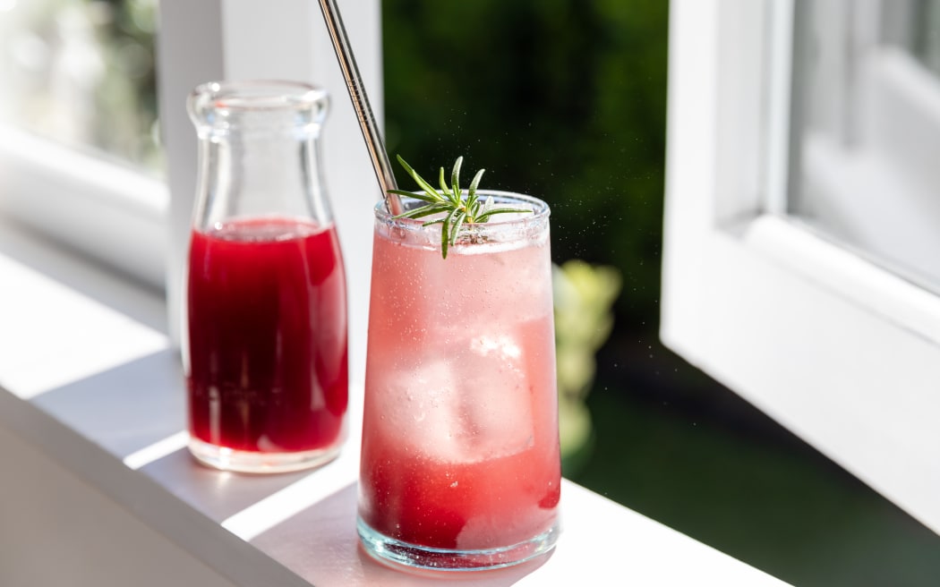Honey and berry shrub cordial in a glass sitting on a windowsill.