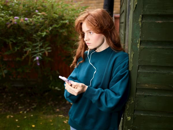 A redhead teenager holds a mobile phone,