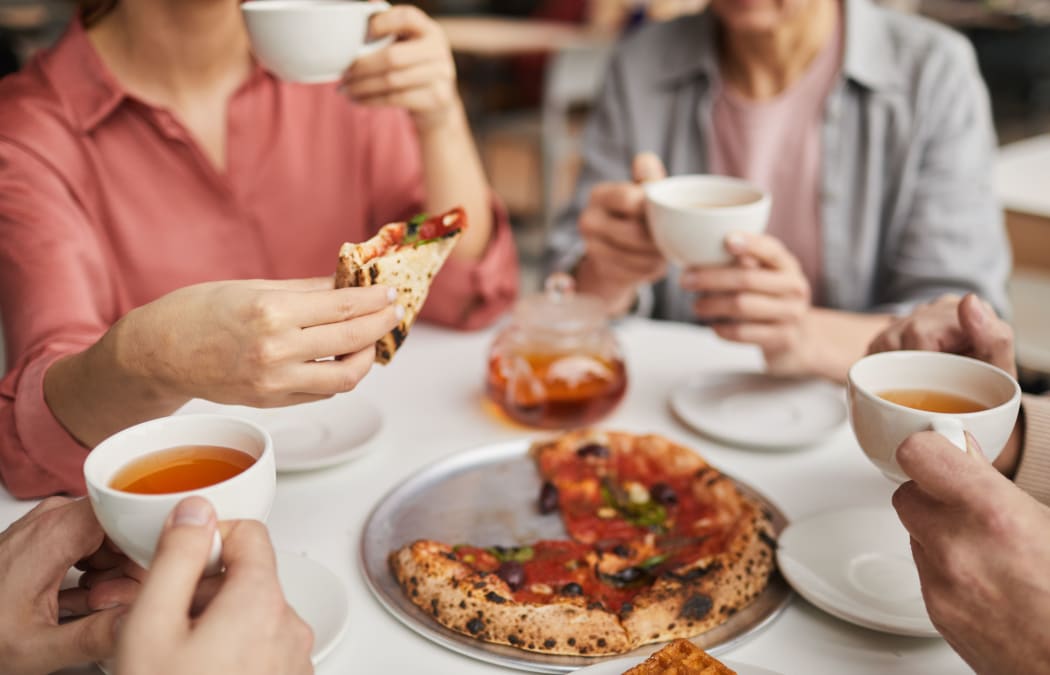 Close-up of woman holding piece of pizza and having lunch together with her family at the table