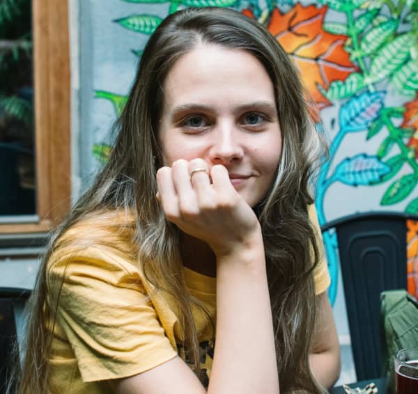A girl with long brown hair and a yellow t-shirt smiles at the camera.