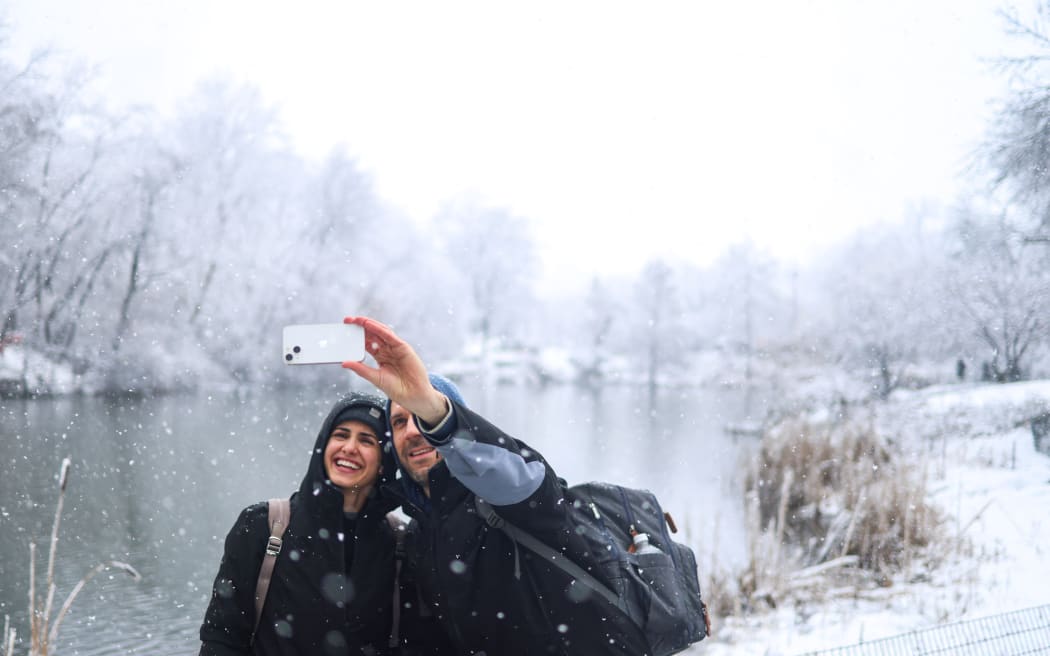 People take a photo as snow falls in Central Park in New York City on February 13, 2024. Millions of people in the northeastern US were engulfed by snow on February 13 as a powerful winter storm battered the region causing flight cancellations and closing schools. (Photo by Charly TRIBALLEAU / AFP)