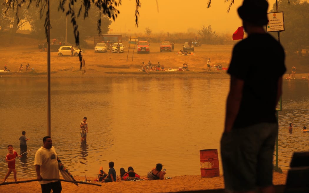 People bathe during the fires in Renaico, Araucania region, Chile on February 4, 2023. - Chile has declared a state of disaster in several central-southern regions after a devastating heat wave provoked forest fires that left four people dead, authorities said on Friday. (Photo by JAVIER TORRES / AFP)