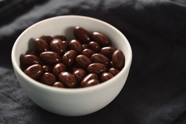 Milk chocolate dragee in white bowl on linen background, shallow focus