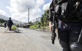 French police officers stand guard on a road in Mont-Dore, a suburb of Noumea, in New Caledonia, on May 28, 2014, while a tow lifts the wreckage of a burned car. Angry residents from the Saint Louis tribal group burned cars creating roadblocks on May 24, 2014