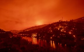 In this long exposure photograph, flames set ablaze both sides of a segment of Lake Berryessa during the Hennessey fire in the Spanish Flat area of Napa, California on 18 August, 2020.