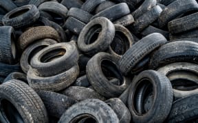Big pile of automobile tires on the broken-down plant. Many black rubber tyres on the ground inside the old huge empty building.