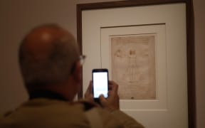 A man takes a picture with mobile phone at the " Vitruvian Man " the famous annotated drawing, made around 1490 with pen, ink and wash on paper, by Leonardo da Vinci's,  during the opening of the exhibition " Leonardo da Vinci ", on October 22, 2019 at the Louvre museum in Paris.