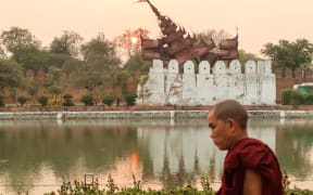 A Buddhist monk walks past the damaged Mandalay Palace during sunset in Mandalay on March 31, 2025, three days after the deadly Myanmar earthquake. Myanmar declared a week of national mourning on March 31 for the country's devastating earthquake, as the death toll passed 2,000 and hopes faded of finding more survivors in the rubble of ruined buildings. (Photo by Sebastien BERGER / AFP)