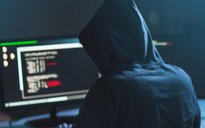 cybercrime, hacking and technology concept - male hacker in dark room writing code or using computer virus program for cyber attack