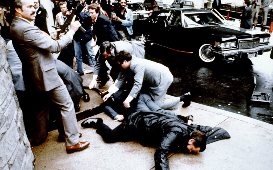 This photo taken by presidential photographer Mike Evens on March 30, 1981 shows police and Secret Service agents reacting during the assassination attempt on then US president Ronald Reagan, after a conference outside the Hilton Hotel in Washington, D.C.. Police officer Thomas Delahanty (foreground) and Press Secretary James Brady (behind) lay wounded on the ground. Reagan was hit by one of six shots fired by John Hinckley, who also seriously injured press secretary James Brady (just behind the car).  Reagan was hit in the chest and was hospitalized for 12 days. Hinckley was aquitted 21 June 1982 after a jury found him mentally unstable. (Photo by MIKE EVENS / CONSOLIDATED NEWS PICTURES / AFP)