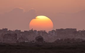This picture taken from a position in southern Israel near the border with the Gaza Strip shows the sun setting behind destroyed buildings in Gaza on March 3, 2024, amid continuing battles between Israel and the Palestinian militant group Hamas. (Photo by Menahem KAHANA / AFP)