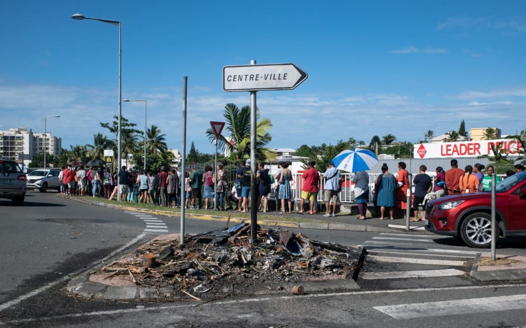 People wait in line to buy provisions from a supermarket as charred items previously set on fire are seen following overnight unrest in the Magenta district of Noumea, France's Pacific territory of New Caledonia, on May 18, 2024. Hundreds of French security personnel tried to restore order in the Pacific island territory of New Caledonia on May 18, after a fifth night of riots, looting and unrest. (Photo by Delphine Mayeur / AFP)