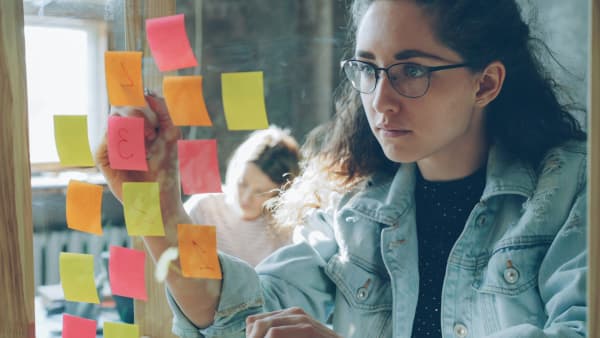 A young girl writes numbers on post-it notes stuck to a mirror.