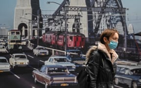 A woman wearing a mask walks past an image of the Sydney Harbour Bridge.