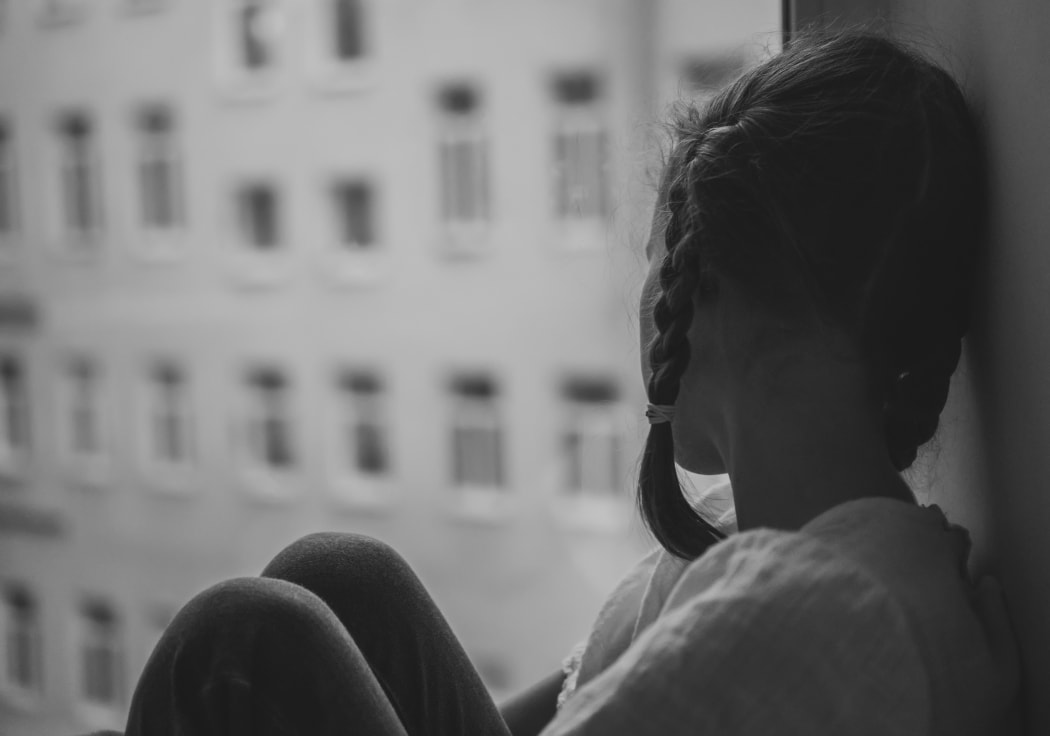 Sad little girl sitting near the window.