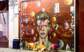 Flowers and candles are left past a mural depicting the cover of Aladdin Sane, to remember the firth anniversary of the death of the British iconic musician David Bowie, in Brixton, south London on January 10, 2021.