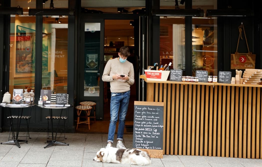 A restaurant employee, wearing a protective mask, uses his phone as he waits for clients to buy takeout lunches, on the fourth day of a lockdown aimed at containing the spread of the novel coronavirus (Covid-19) in Paris.