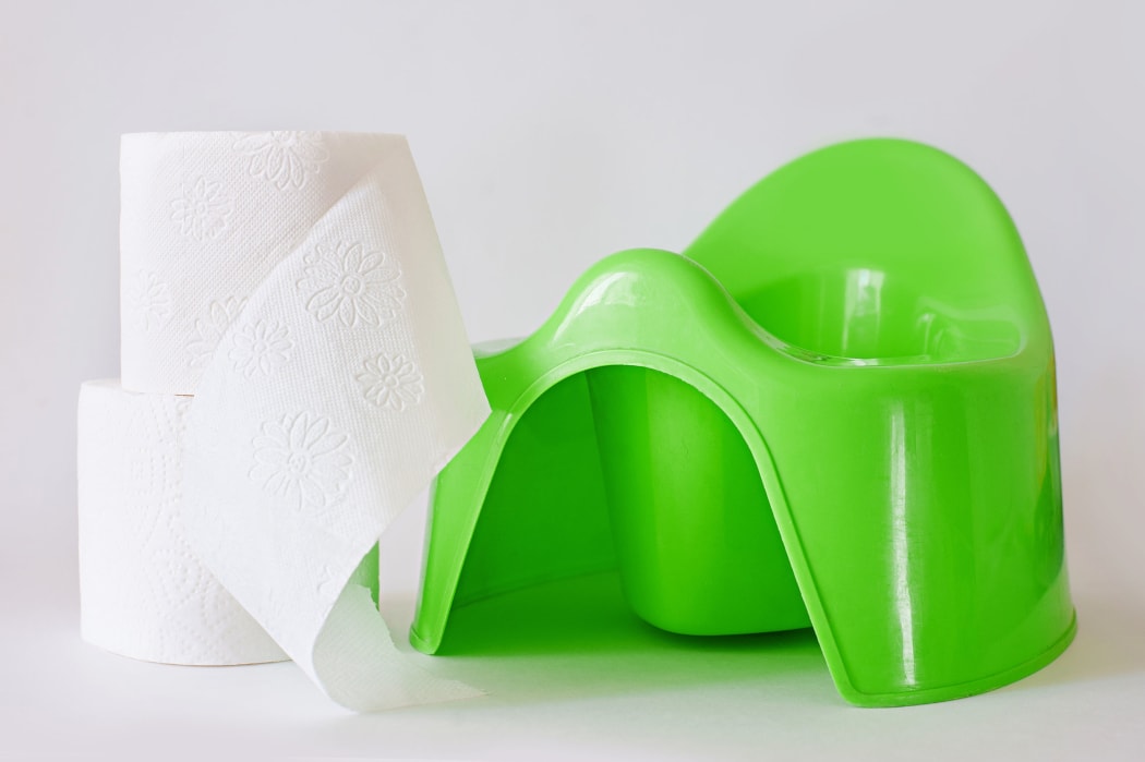 A photo of a childrens green potty and toilet paper on a white background