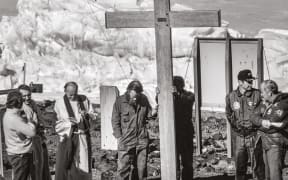 The dedication service of the crash memorial cross took place in front of Scott Base shortly after everyone had evacuated the crash site. From left: Mike Prebble, leader of Scott Base, talks to two US Navy chaplains; Garth Varcoe and Ted Robinson hold the cross; US Navy Commander Darryl Westbrook; and Bob Thomson, superintendent of DSIR Antarctic Division.