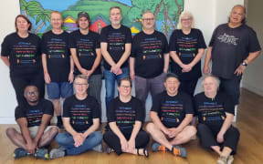 The New Zealand Scrabble team pose for a photo in two rows, all smiling at the camera and wearing team shirts.