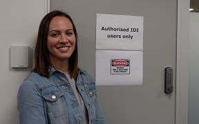Young women stands outside door with sign saying "Authorised  IDI users only" and "warning" only  nerds beyond thispoint