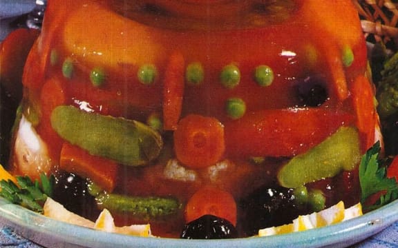 A close up photo of a 70s dish in which carrots, peas and other vegetables are encased in a mound of jelly.