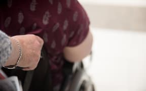 A mother pushes her adult daughter around a shopping mall in a wheelchair.