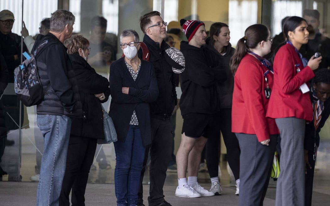 Evacuated people stand outside a terminal after a gunman opened fire at the airport in Canberra on August 14, 2022. - A gunman fired about five shots inside Canberra's main airport on August 14, sending passengers fleeing but injuring no-one before he was detained by Australian police. (Photo by AFP)