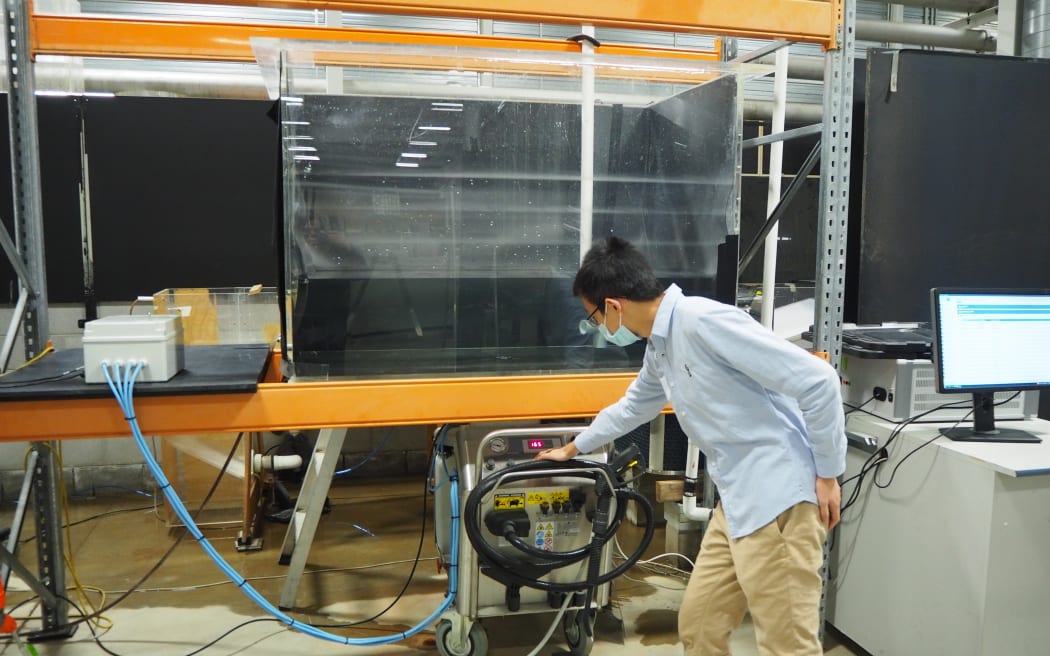 Dr. Yaxiong Shen switches on the air compressor to start an experiment. There is a large perspex tank of water with the compressor below it.