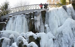 People standing on a bridge above a frozen waterfall at the Bergpark Wilhelmshoehe park in Kassel in central Germany.