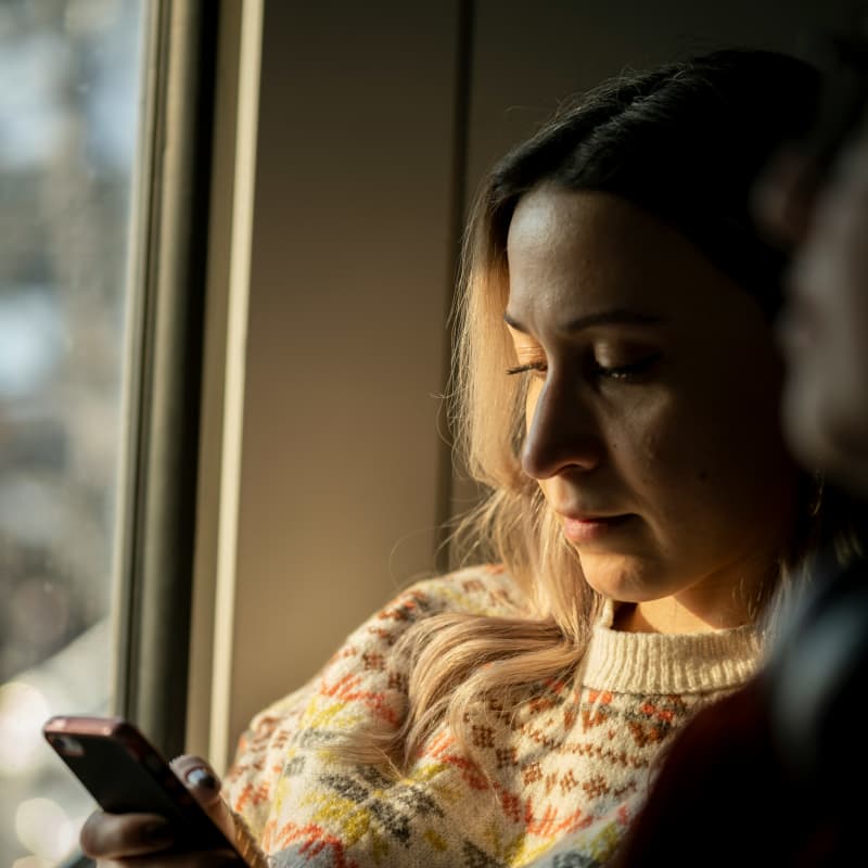 A blonde woman in soft light looks down at her phone.