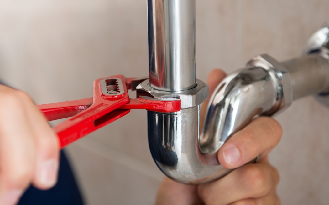 A plumber fixes a pipe with a wrench.